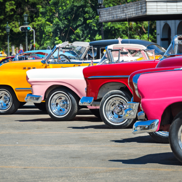 Classic sports cars parked in a lot at a car show, with various wraps and colors.