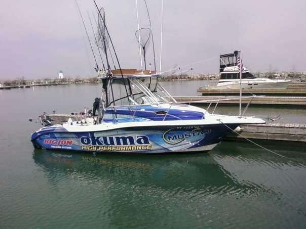 A boat with a fishing pole on it, featuring a boat wrap with the text "Okuma."