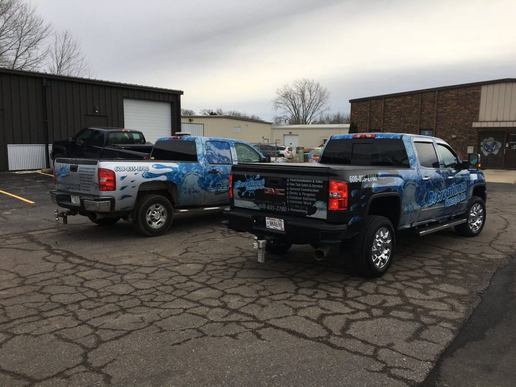 Two trucks parked in front of a building, showcasing their distinct colors and designs against the urban backdrop.