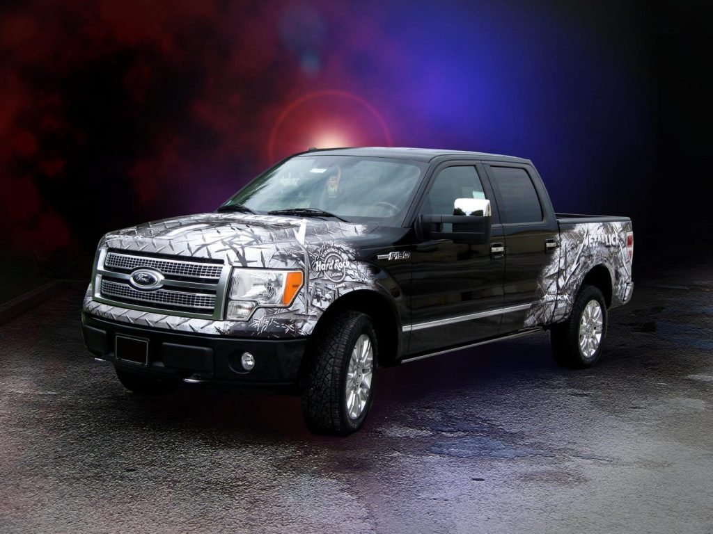A Ford truck featuring a camouflage wrap, blending seamlessly with its surroundings in an outdoor setting.