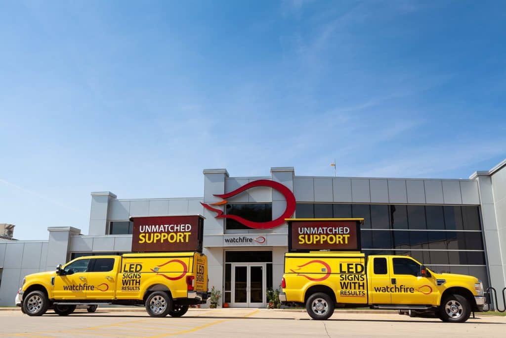 Two yellow trucks are stationed in front of a building, highlighting their bright appearance in the city environment.